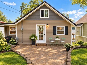 Une maison de plain-pied avec un porche à l’avant, un paillasson et un petit patio avec deux chaises.