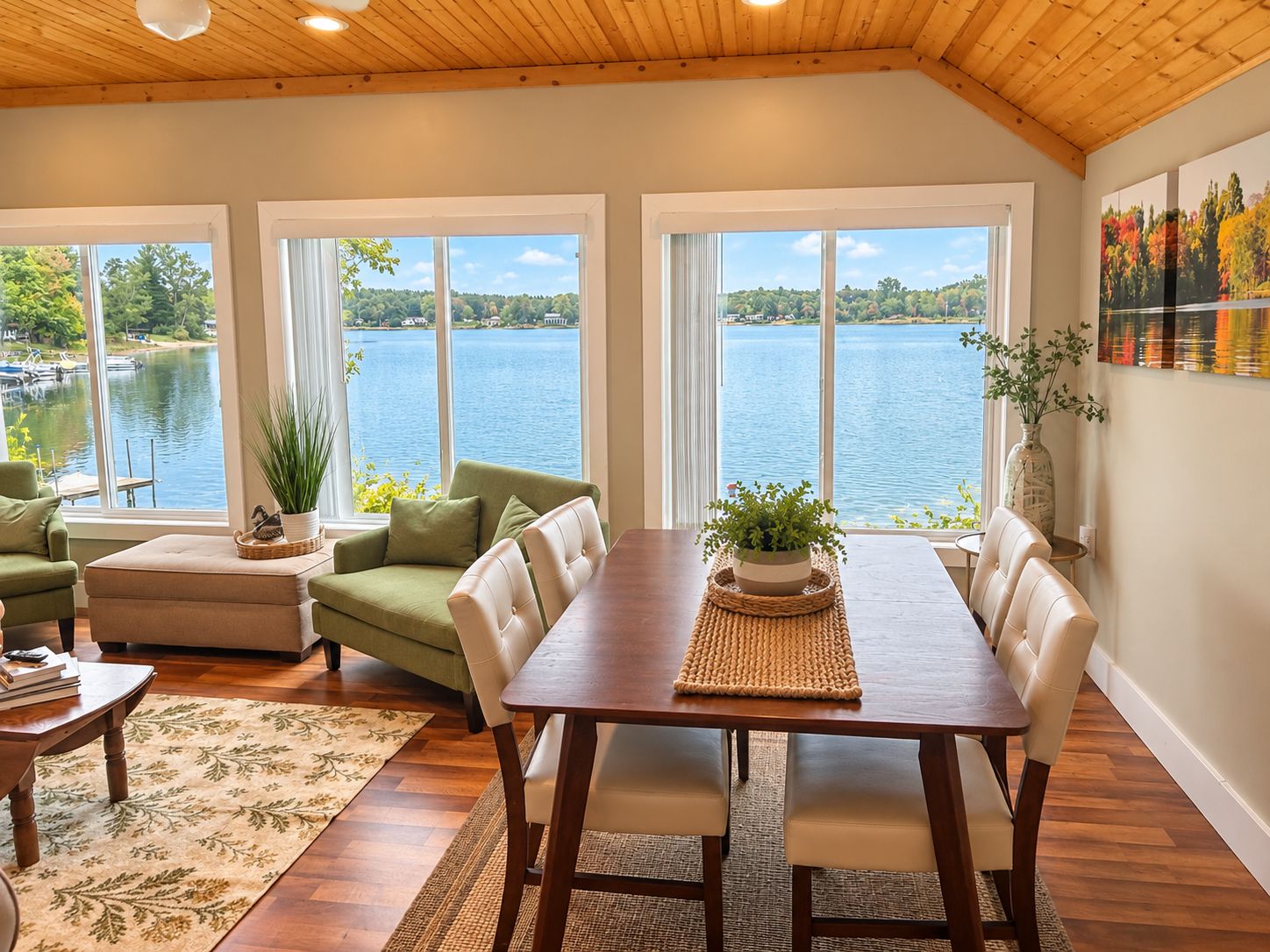 Une pièce spacieuse avec un plafond en bois, de grandes fenêtres donnant sur un lac, une table à manger avec des chaises et un canapé vert.