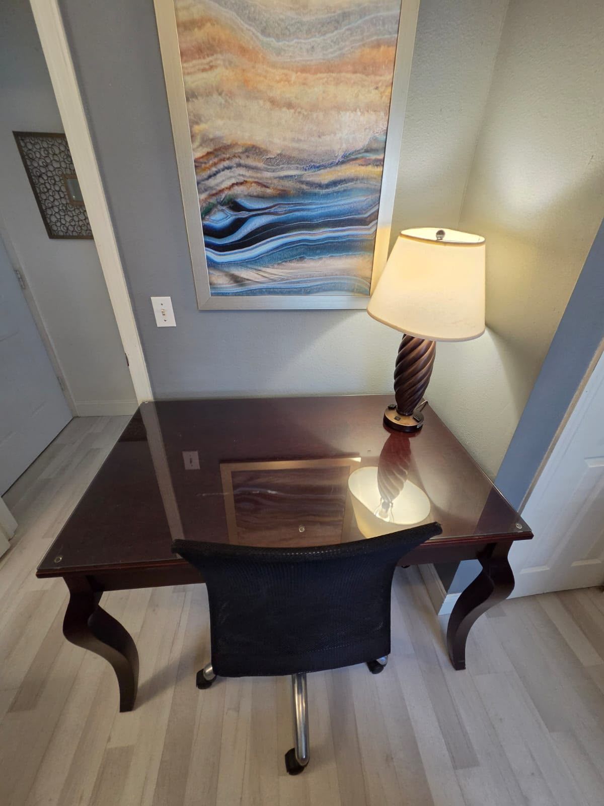 Un bureau avec une lampe, une chaise et un mur orné d’un tableau.