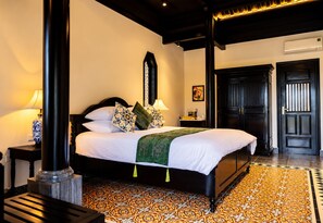 Quarto de hotel com uma cama grande, mesa de cabeceira, luminária, quadro e uma porta.