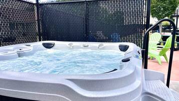 A hot tub with a black fence enclosure, a green chair, and a patio area.