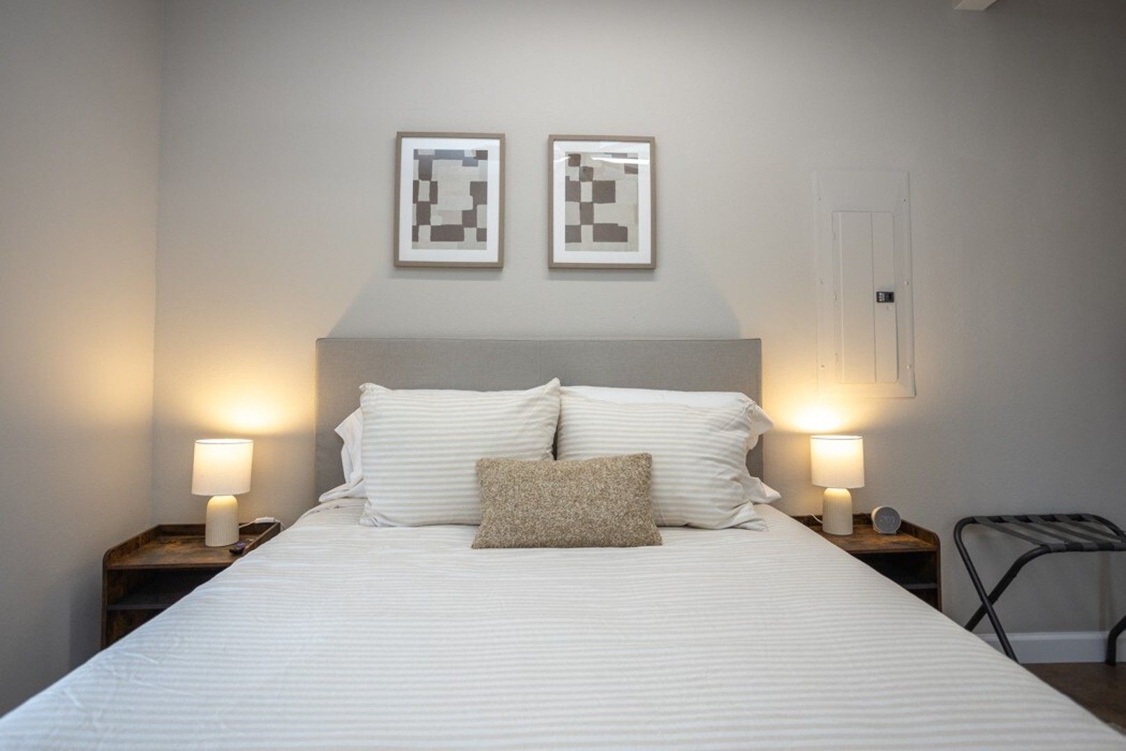 A neatly made bed with white bedding and two pillows, flanked by bedside tables with lamps, in a room with a simple, clean design.