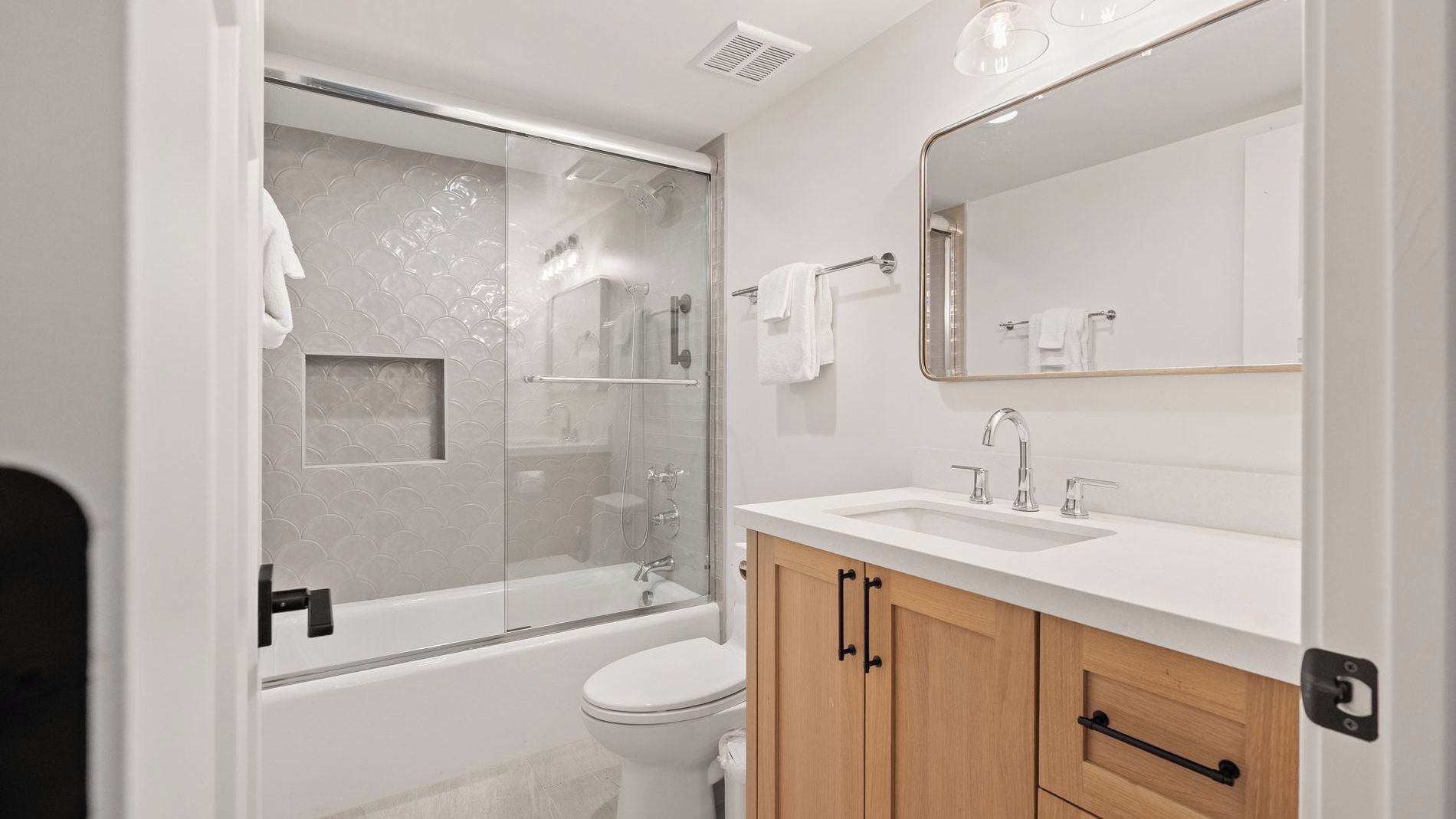A modern bathroom with a glass-enclosed shower, a white sink, and wooden cabinets.