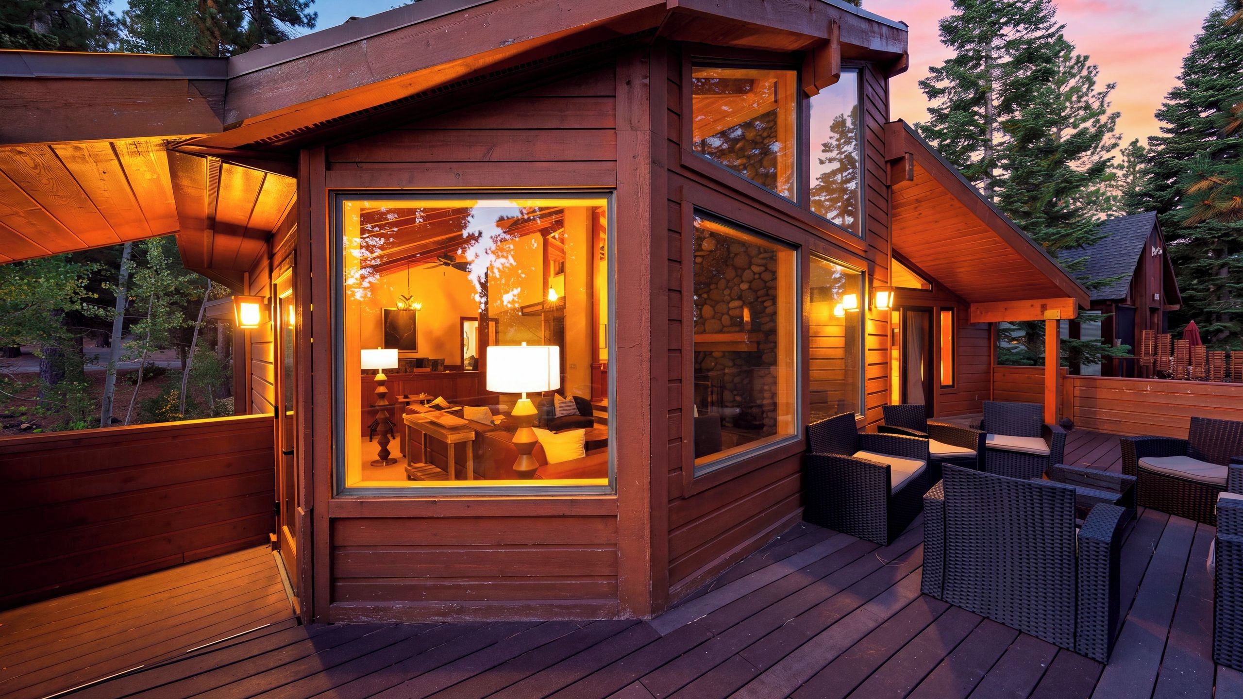 Une cabane en bois dotée de grandes fenêtres, d’une terrasse et de mobilier d’extérieur.