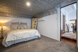 A bedroom with a bed, a lamp, a wall-mounted device, and a carpeted floor.