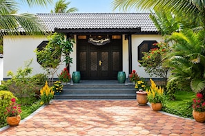 Een villa met een pannendak, zwarte deuren en een bord met de tekst 'Coconut Garden Villa'.