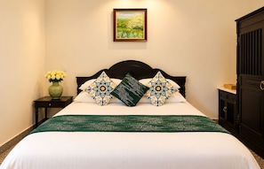 Een net opgemaakt bed met een witte lakenset en een beddekleed met een groen patroon, omlijst door twee decoratieve kussens met ingewikkelde dessins.