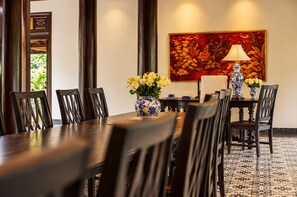 Un coin repas avec une longue table, des chaises, un vase de fleurs, une lampe et un tableau accroché au mur.