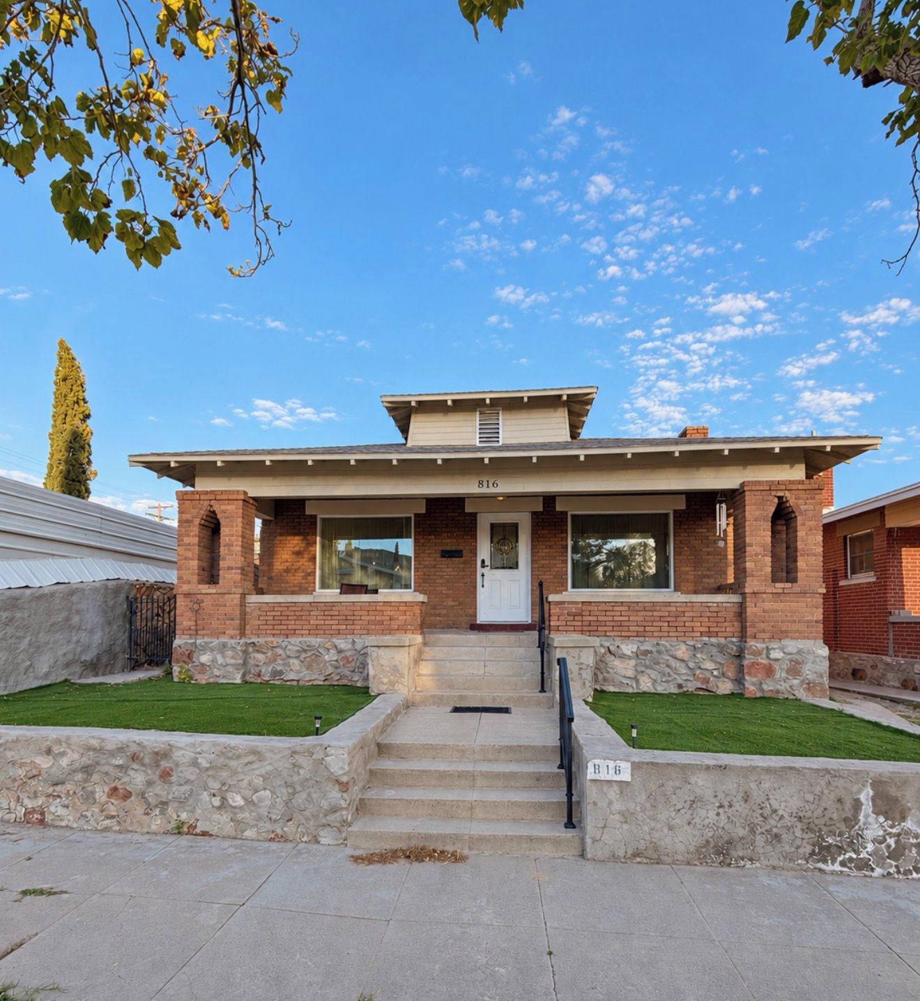 A two-story brick house with a front porch, a stone foundation, and a clear blue sky.