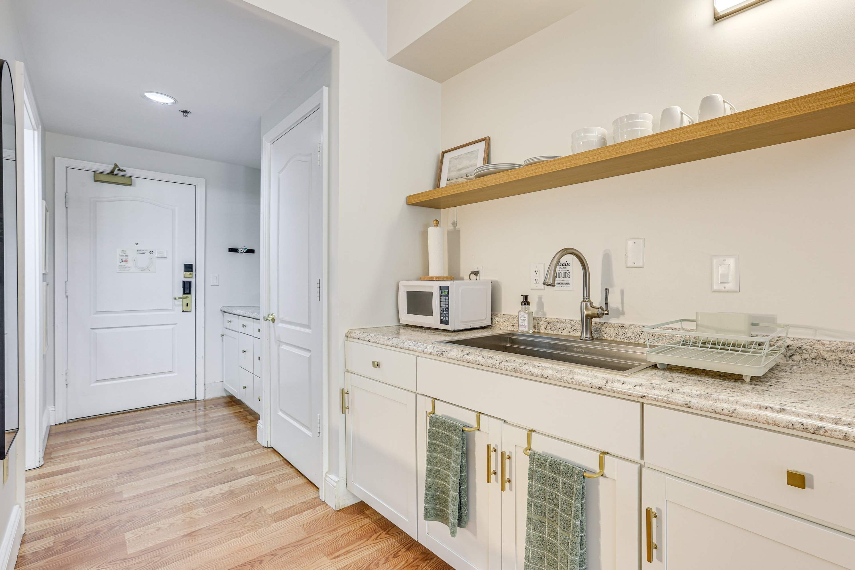 A kitchen with a microwave, sink, and wooden shelf above.