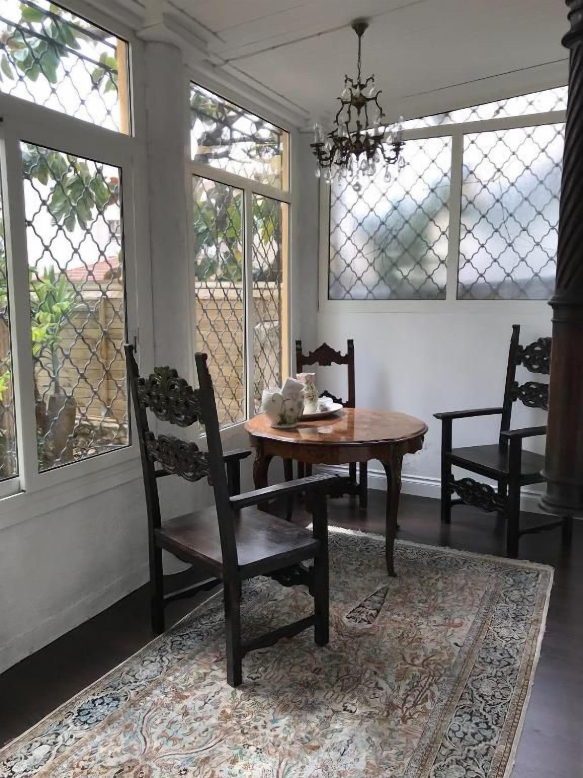 Una habitación con una mesa redonda, dos sillas, un tapiz estampado y ventanas amplias con vistas al exterior.