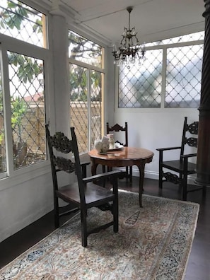 Ein Zimmer mit einem runden Tisch, zwei Stühlen, einem gemusterten Teppich und großen Fenstern mit Blick nach draußen.