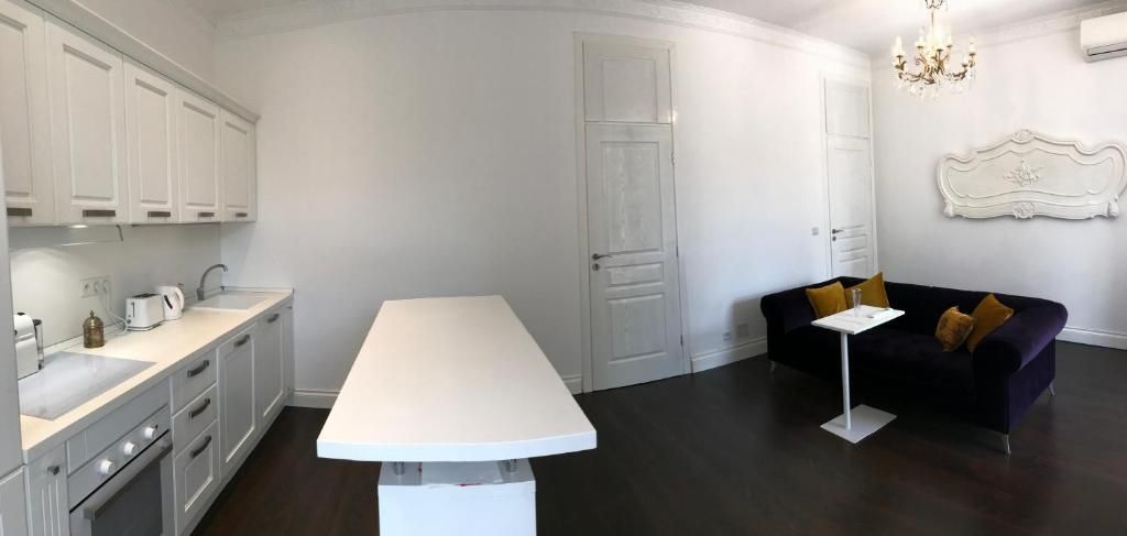 A modern kitchen with white cabinetry, a central island, and a dining area with a dark sofa and cushions.