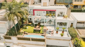 Un edifici modern de diverses plantes amb piscina al terrat, zona de seients a l'aire lliure i vegetació exuberant.
