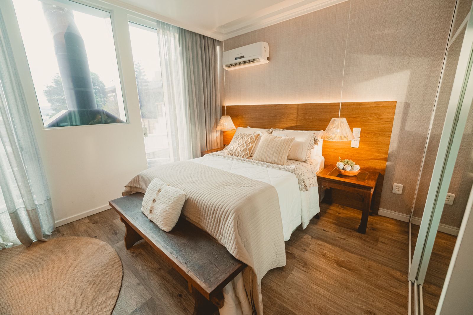 A hotel room with a bed, bedside lamps, a bench, and a view of the outside.