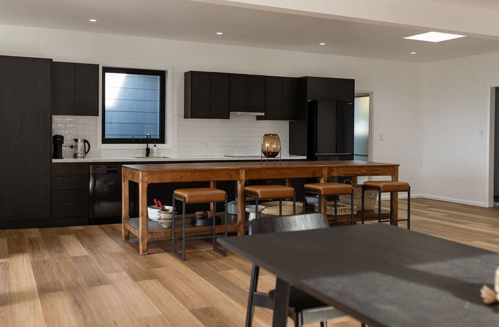 A modern kitchen with dark cabinetry, a wooden island with stools, and a large window.