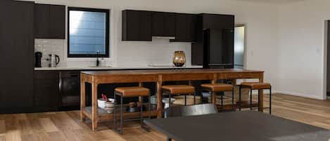 A modern kitchen with dark cabinetry, a wooden island with stools, and a large window.
