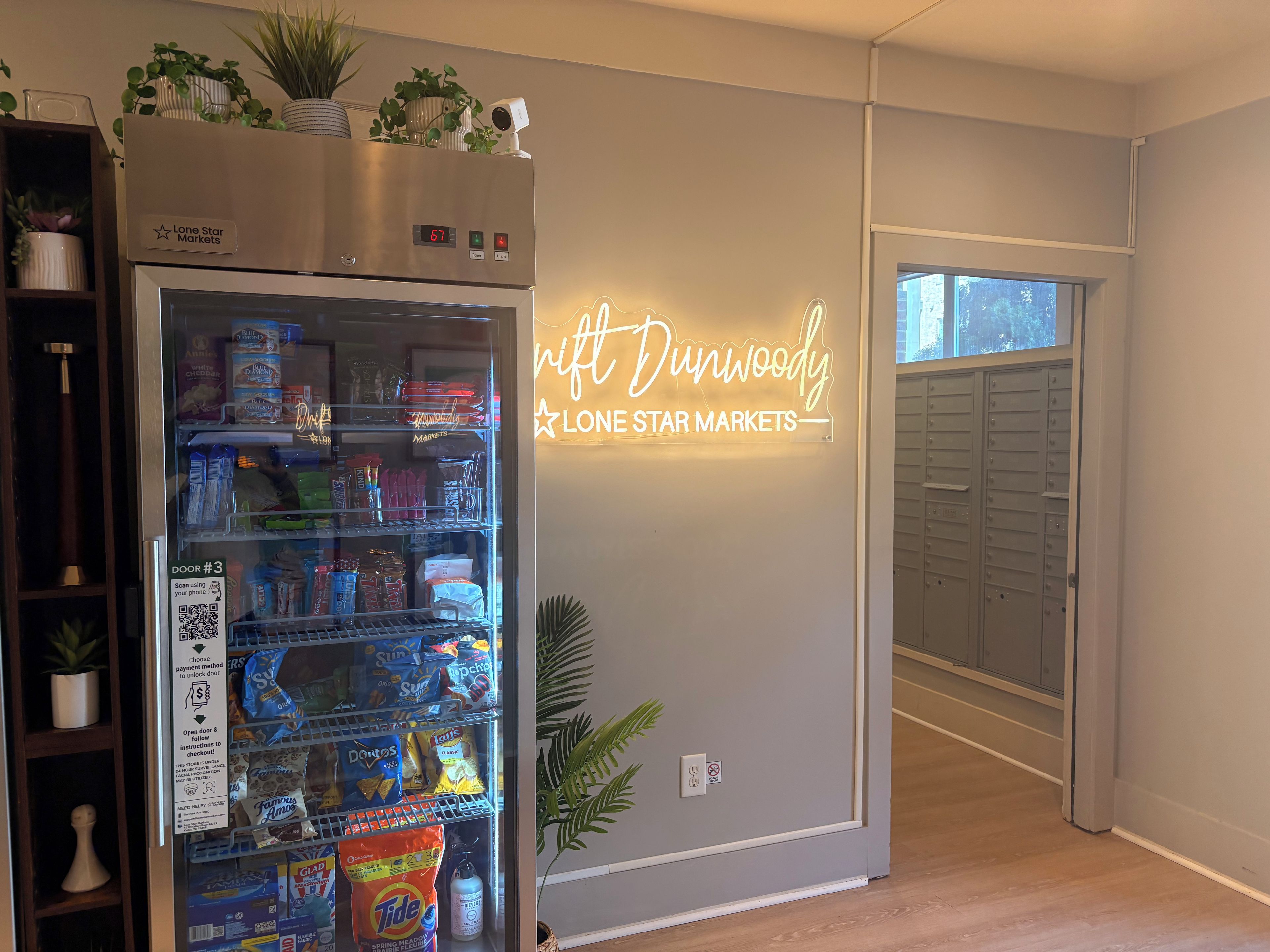 A room with a refrigerator stocked with snacks, a neon sign reading 'Lone Star Markets,' and a door marked 'DOOR #3' with a QR code.