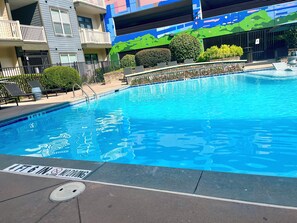 Une piscine à l’eau d’un bleu limpide, entourée d’un mur de pierre et d’une clôture métallique.