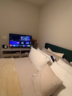 Une chambre d’hôtel avec un lit, des oreillers, un téléviseur posé sur un meuble et une prise de courant au mur.