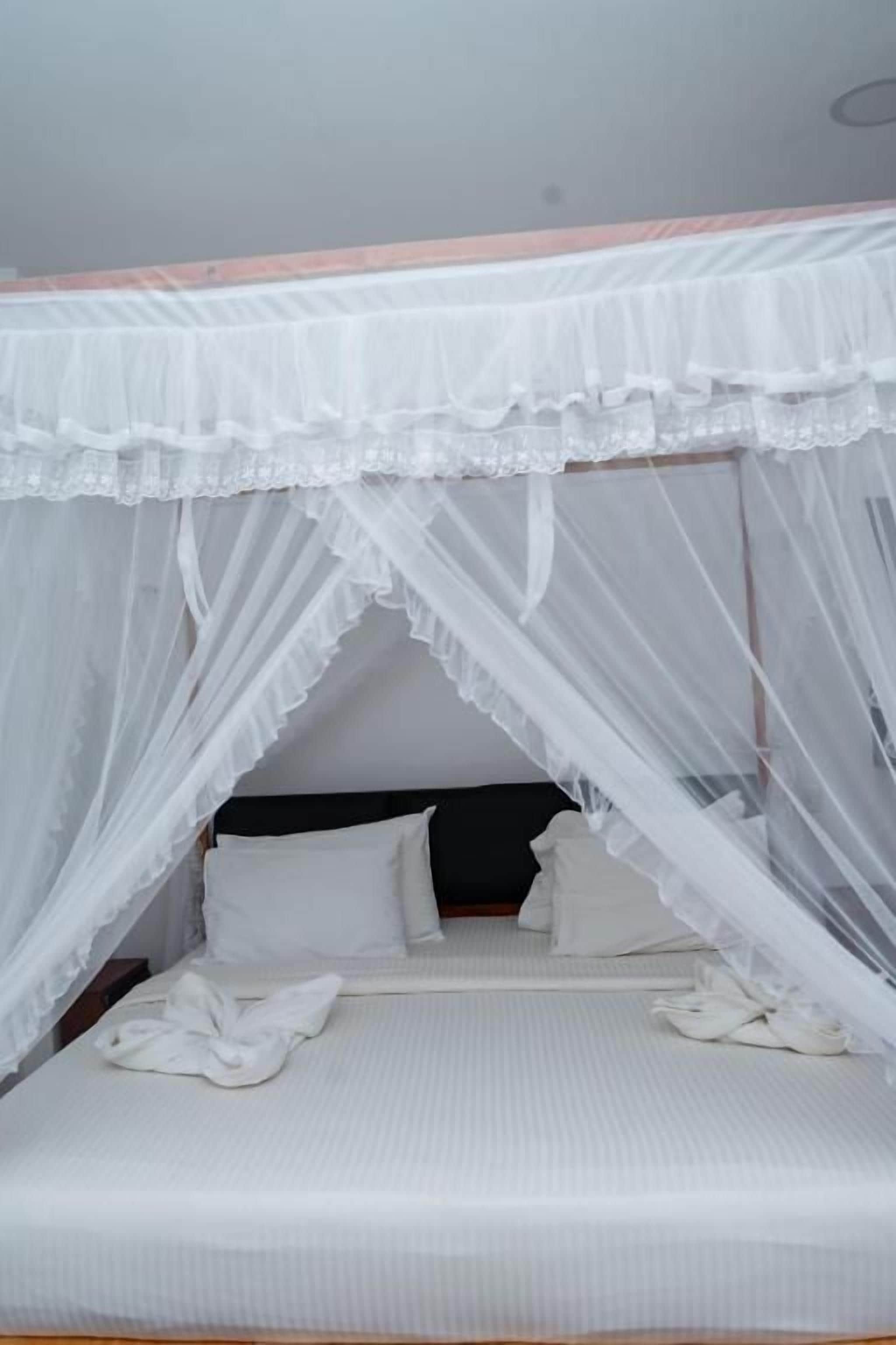 A single bed with a white bedspread and pillows, under a white canopy.