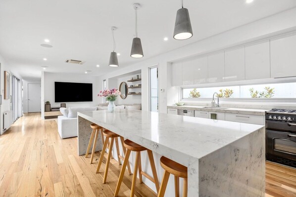 Una cucina moderna con isola in marmo, sgabelli di legno e un'ampia finestra.