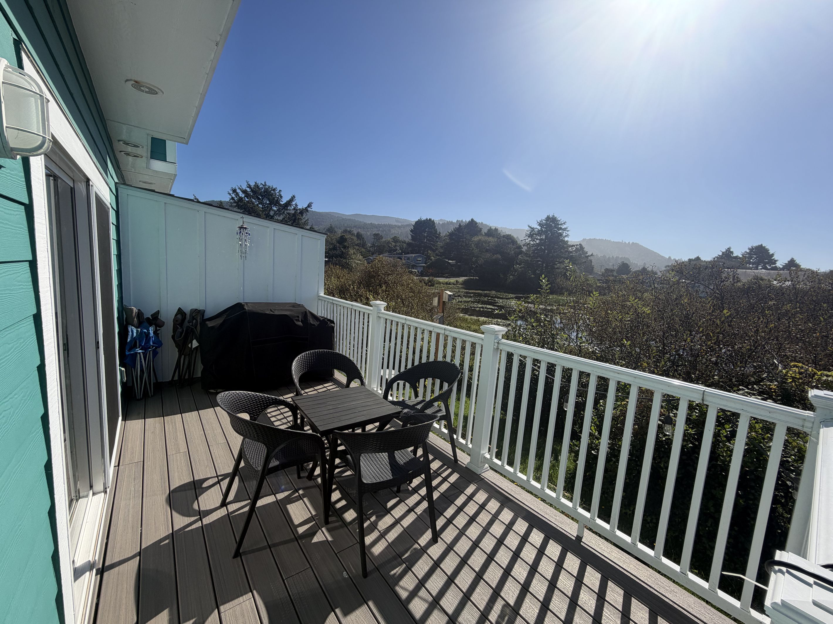 A wooden deck with outdoor furniture, a barbecue grill, and a white railing.