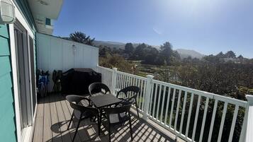 A wooden deck with outdoor furniture, a barbecue grill, and a white railing.