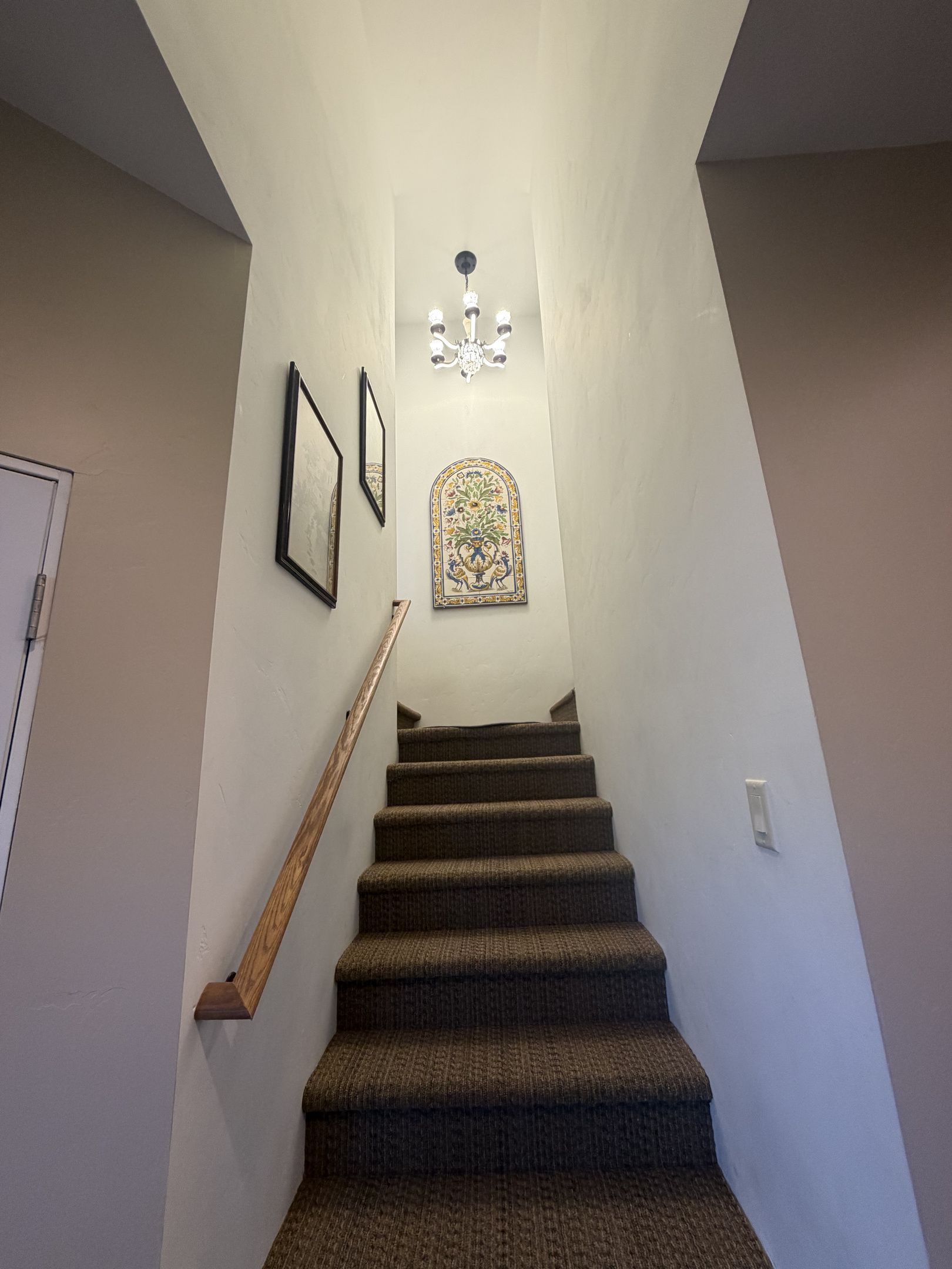 A staircase with a handrail, a wall-mounted light fixture, and a framed decorative plate.
