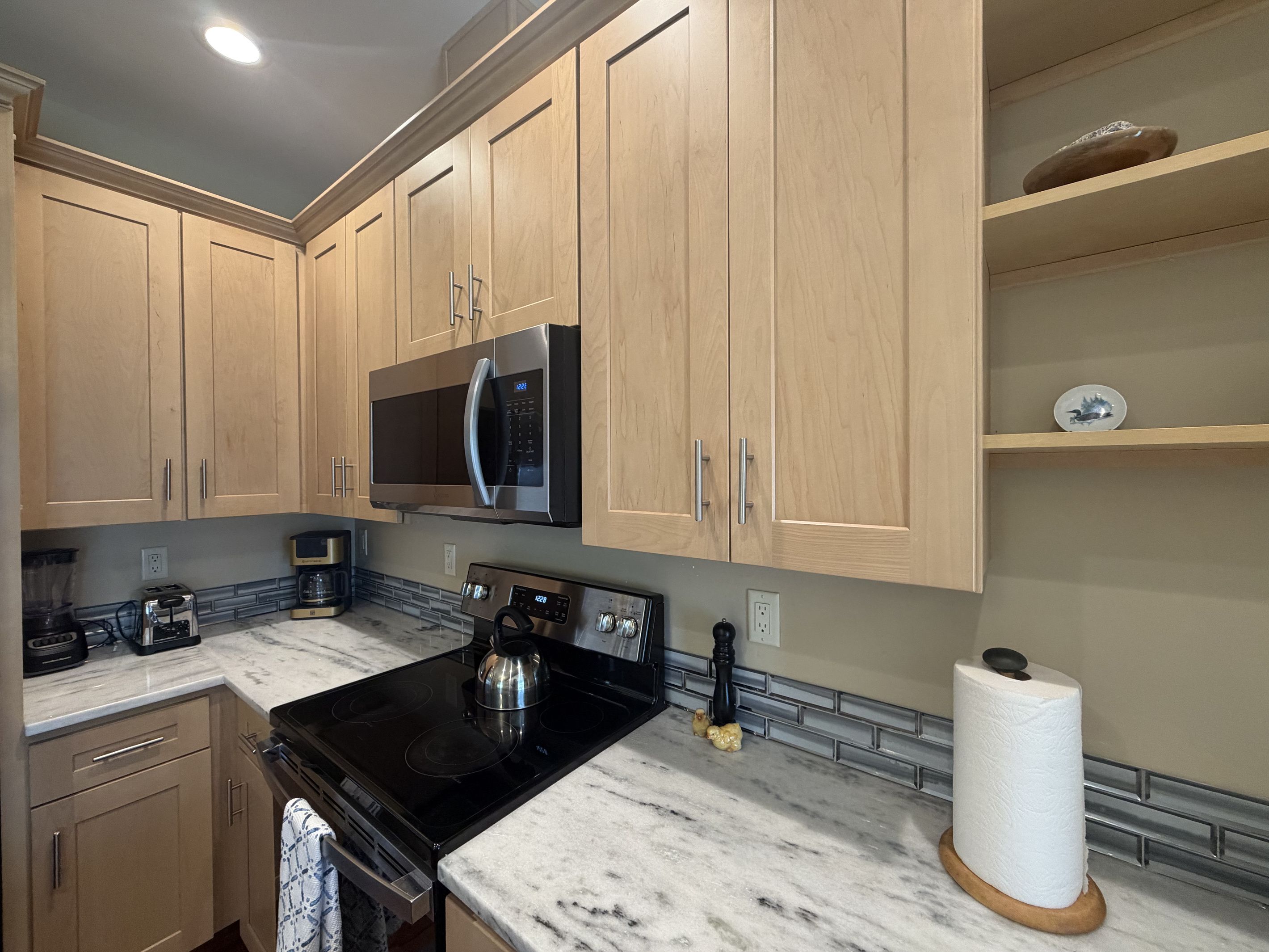 A kitchen with wooden cabinets, a black stove, a microwave, and a marble countertop.