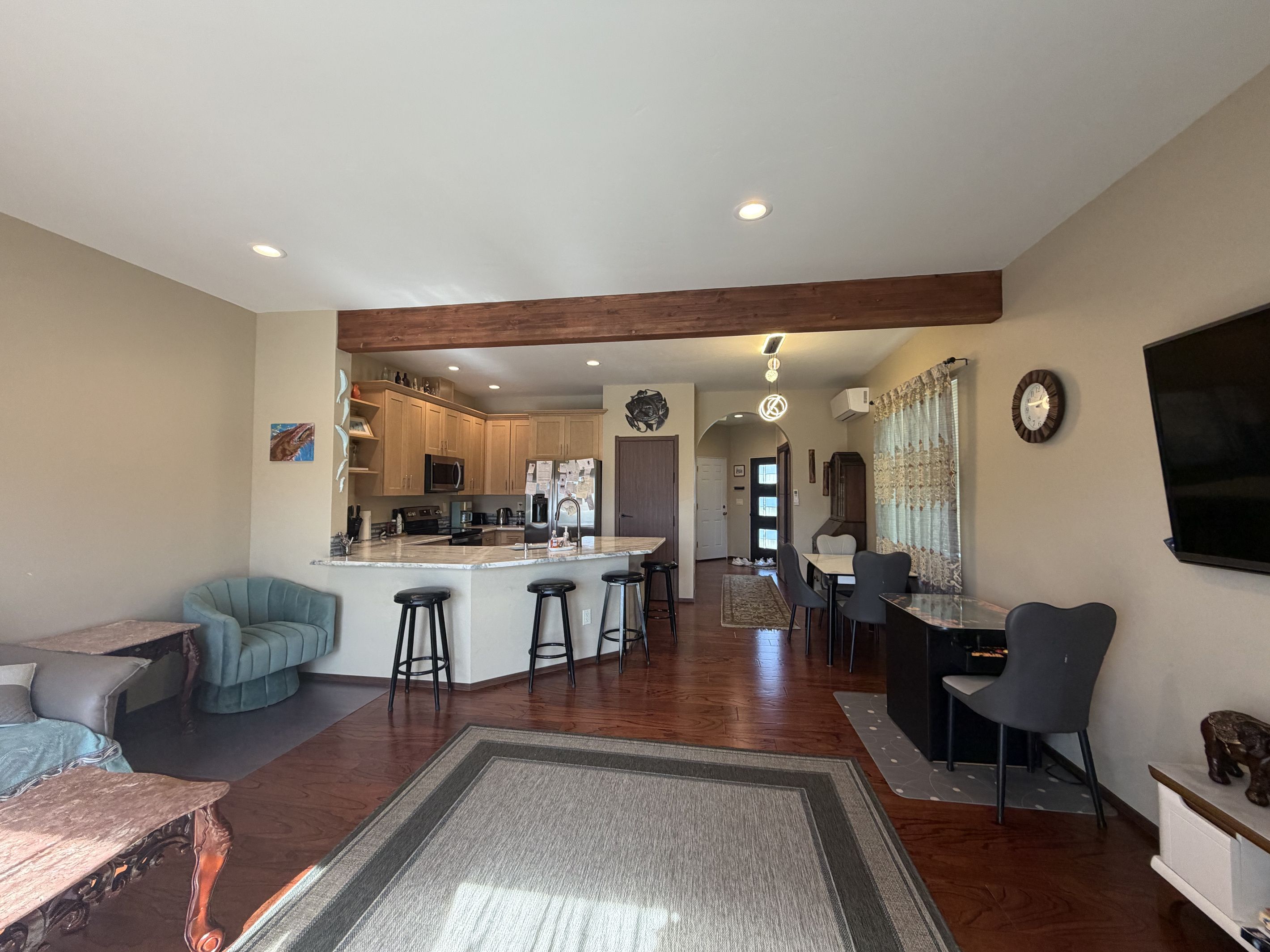 A spacious living area with a kitchen in the background, a dining area with a table and chairs, and a large TV mounted on the wall.