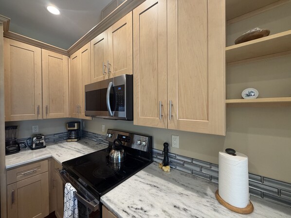 A kitchen with wooden cabinets, a black stove, a microwave, and a marble countertop. - Lake Marie Retreat (East&West) (Rockaway Beach)