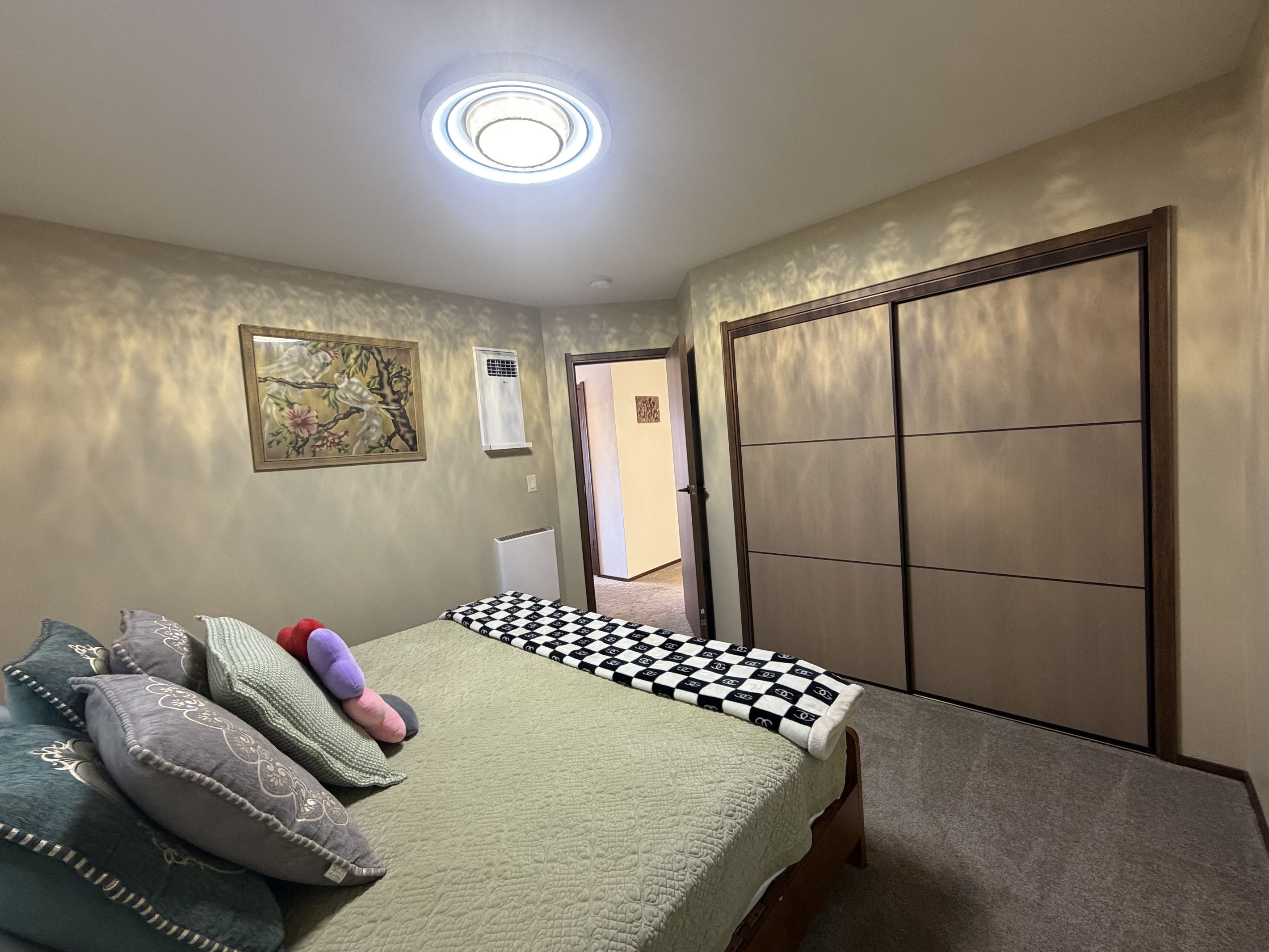 A bedroom with a bed, pillows, a radiator, a window, and a door.