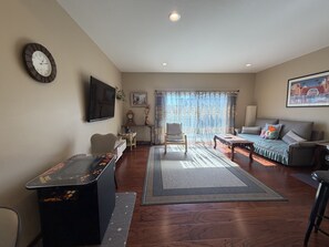 A living room with a sofa, armchair, coffee table, and a TV mounted on the wall. - Lake Marie Retreat (East&West) (Rockaway Beach)