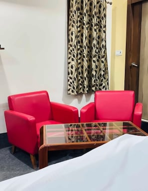 Um quarto com um sofá vermelho, uma mesa de centro de vidro e uma cortina estampada.