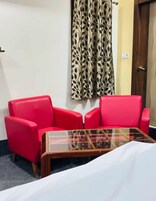 Una habitación con un sofá rojo, una mesa de centro de cristal y una cortina estampada.