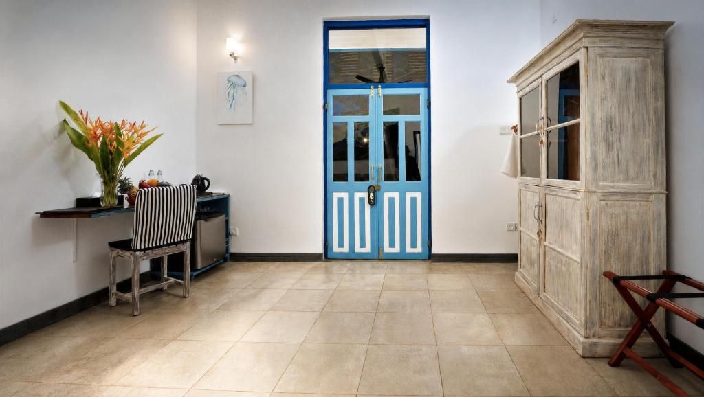 Un pasillo con una puerta azul, un armario de madera, una silla y una pequeña mesa con un jarrón de flores.