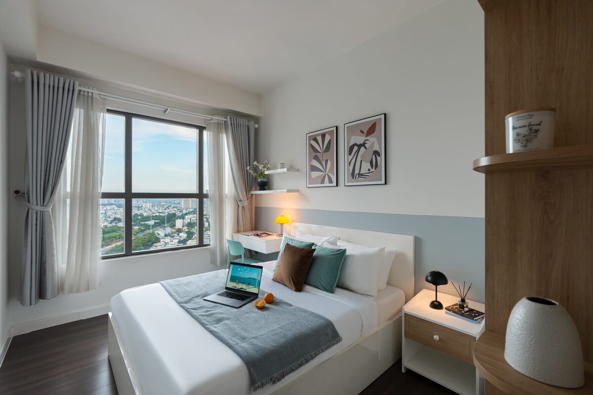 Et moderne hotelværelse med en stor seng, et skrivebord, en lampe og udsigt over byen.