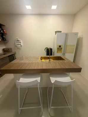 Una cocina moderna con una isla central, dos taburetes de bar, un refrigerador y un microondas.