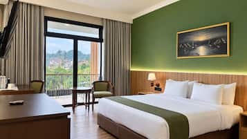 A hotel room with a large bed, a desk, a chair, a nightstand, and a painting on the wall.