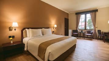 A hotel room with a large bed, bedside lamps, a desk with a chair, and a window with curtains.