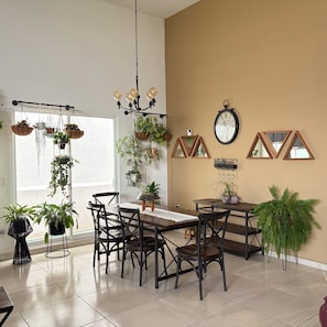 Un comedor con una mesa de madera, sillas negras, plantas colgantes, una araña y espejos en la pared.