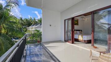 A balcony with a glass door leading to a bedroom with a bed and a small table.