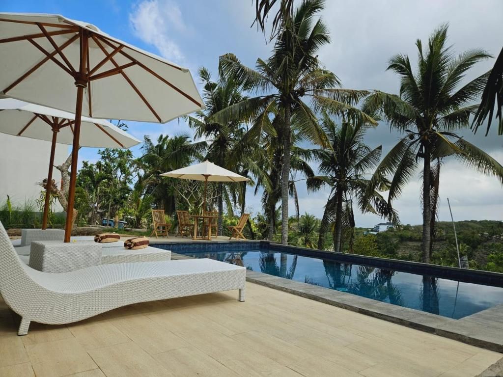 A poolside area with a lounge chair and umbrella, surrounded by palm trees.