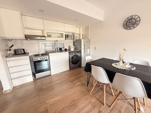 A modern kitchen with white cabinetry, a dining table with chairs, and a wall-mounted clock. - New Listing (San Nicolás de Los Arroyos)