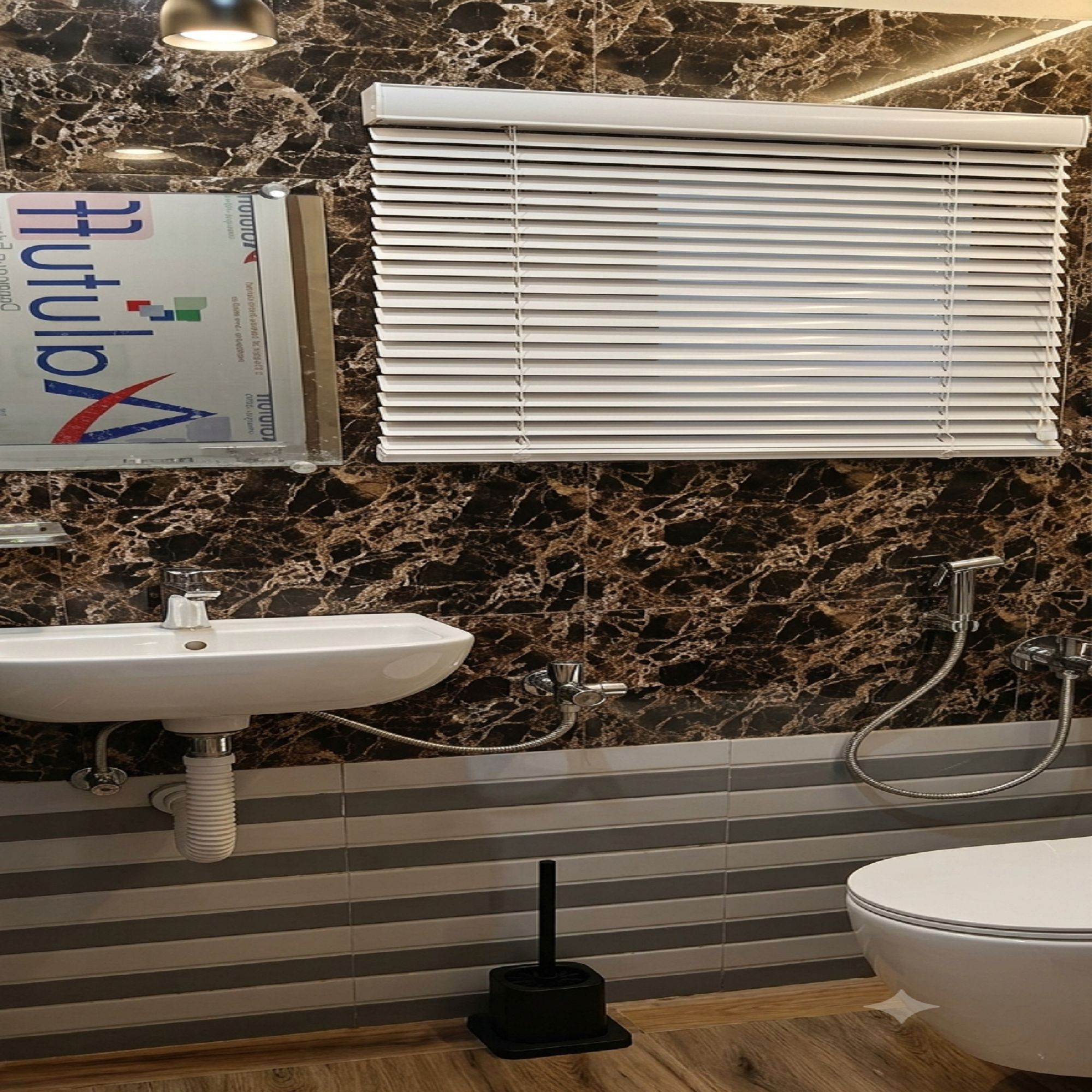 Une salle de bain avec un pare-baignoire en marbre, un lavabo blanc, des toilettes et une douche équipée d’un pommeau de douche à main.