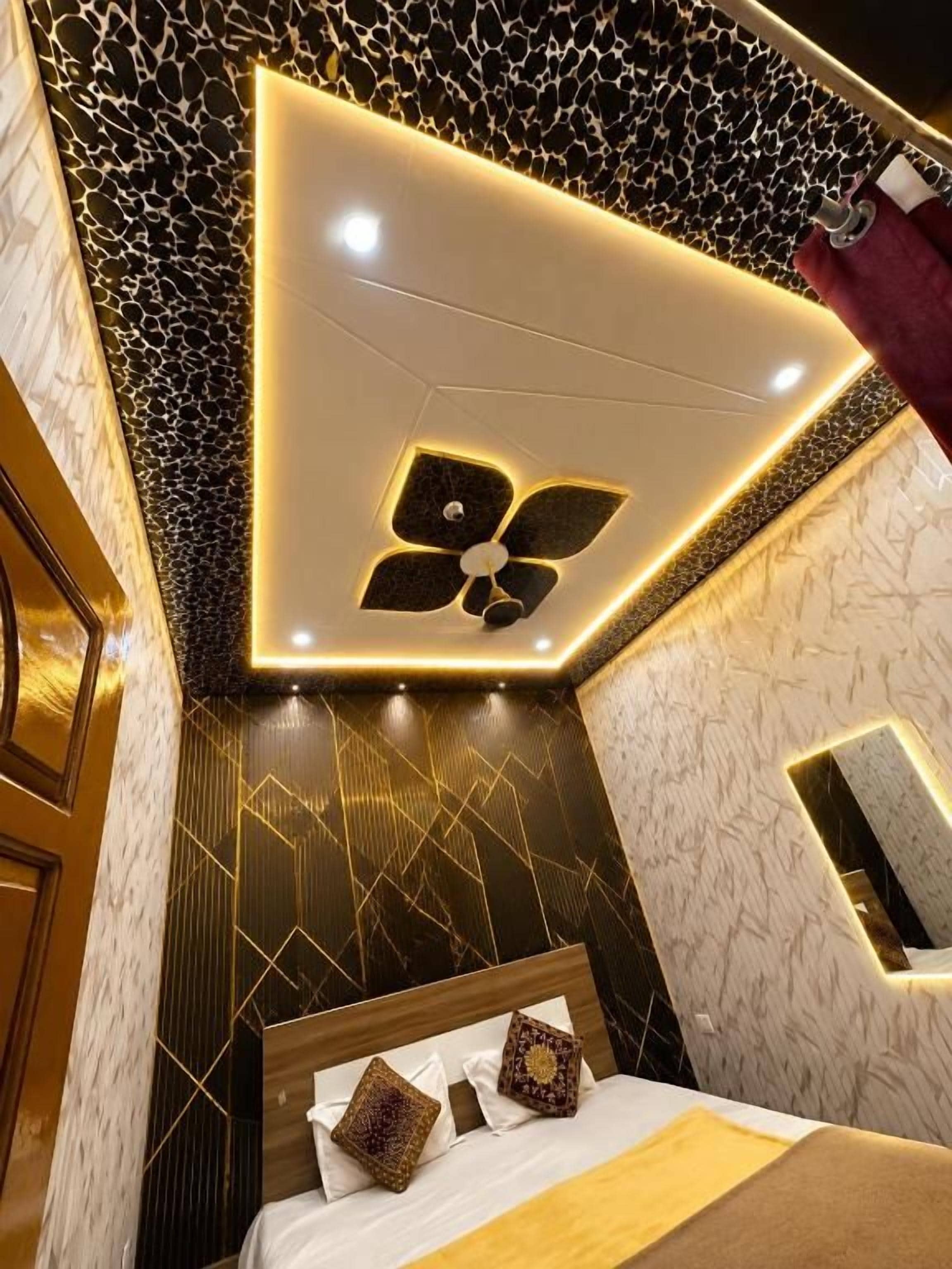 A modern bedroom with a geometric ceiling design, a bed with patterned pillows, and a wall-mounted mirror.