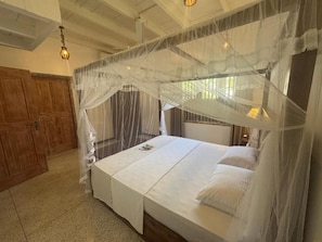 A bedroom with a canopy bed, wooden wardrobe, and a chandelier. - White on White (Hikkaduwa)