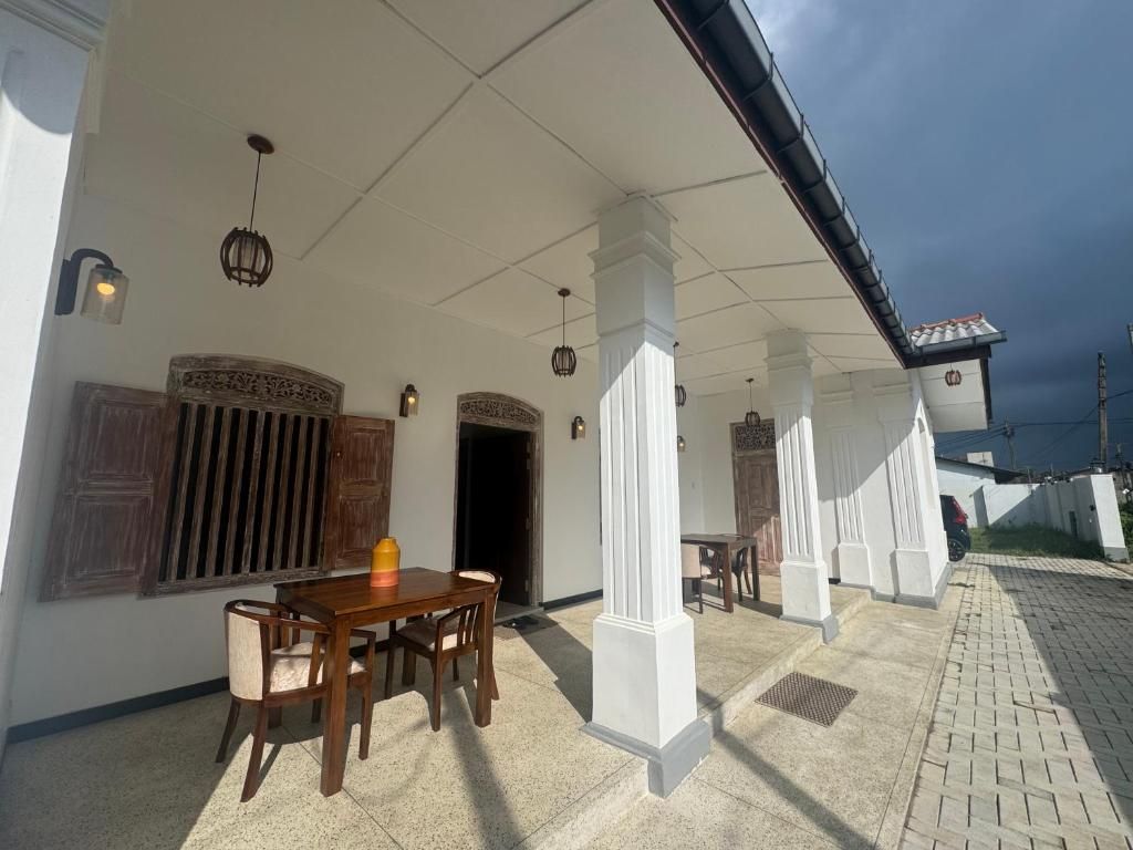 Eine überdachte Terrasse im Freien mit einem Holztisch und Stühlen, weißen Säulen und einem gefliesten Boden.