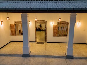A building entrance with a tiled roof, two columns, and wooden doors with glass panels. - White on White (Hikkaduwa)
